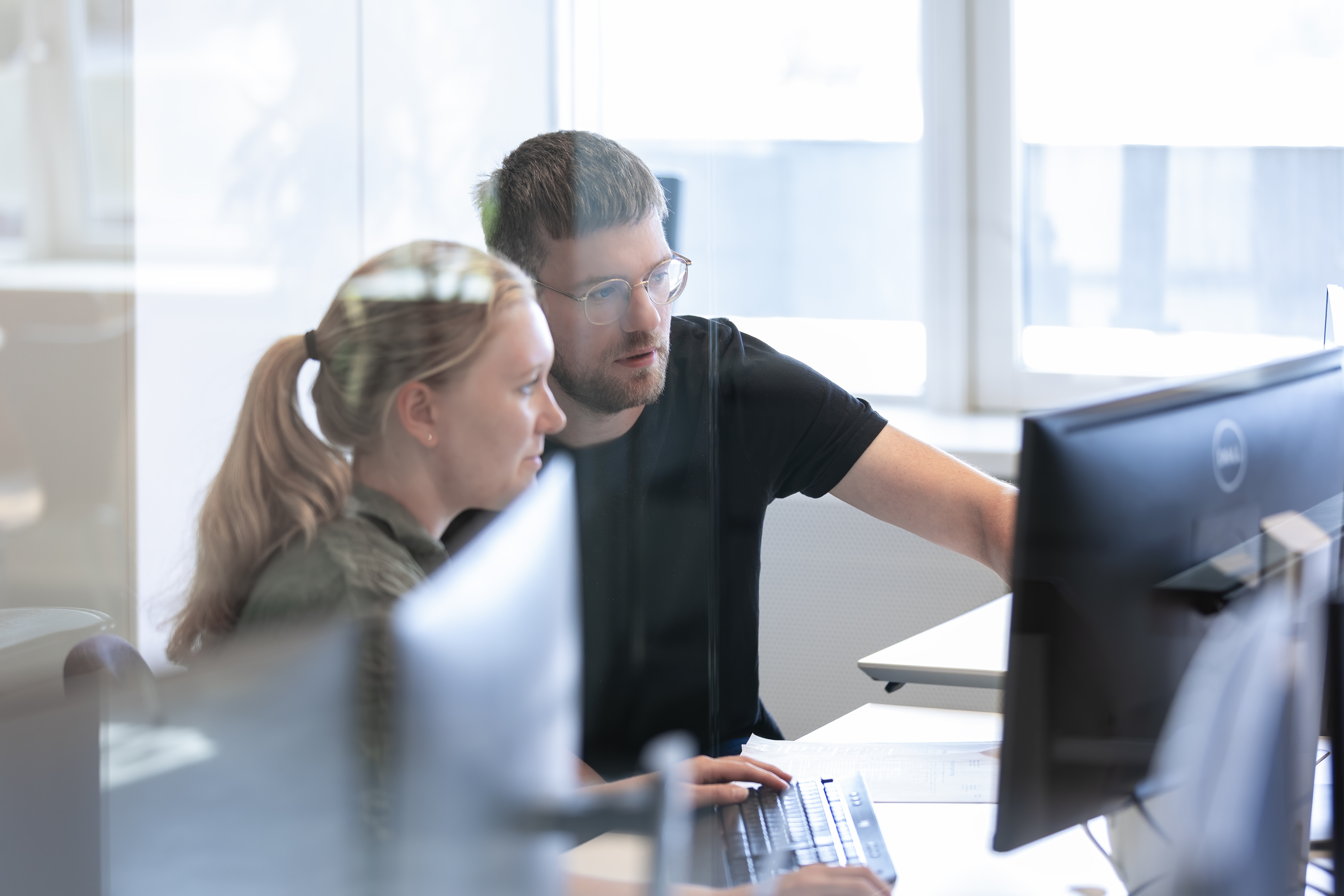 En mand og kvinde sidder ved et skrivebord på et kontor og peger på en computerskærm