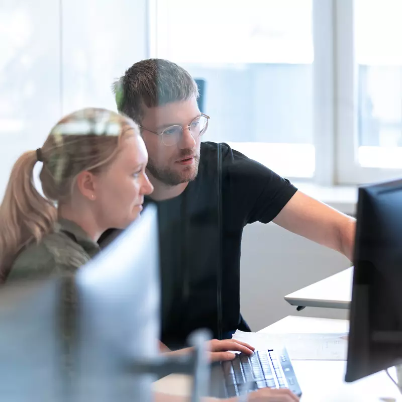 En mand og kvinde sidder ved et skrivebord på et kontor og peger på en computerskærm