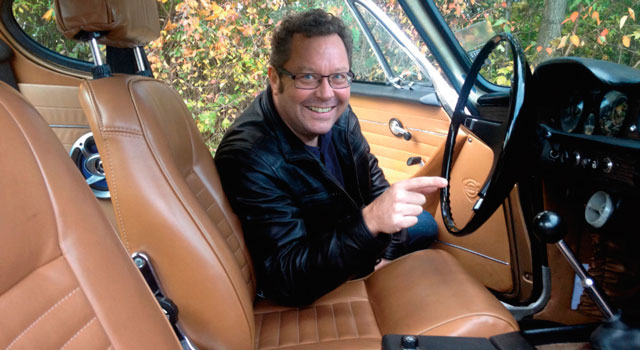 Veteranbil set indefra. Man ser en mand der er glad og som sidder på førersædet i bilen.