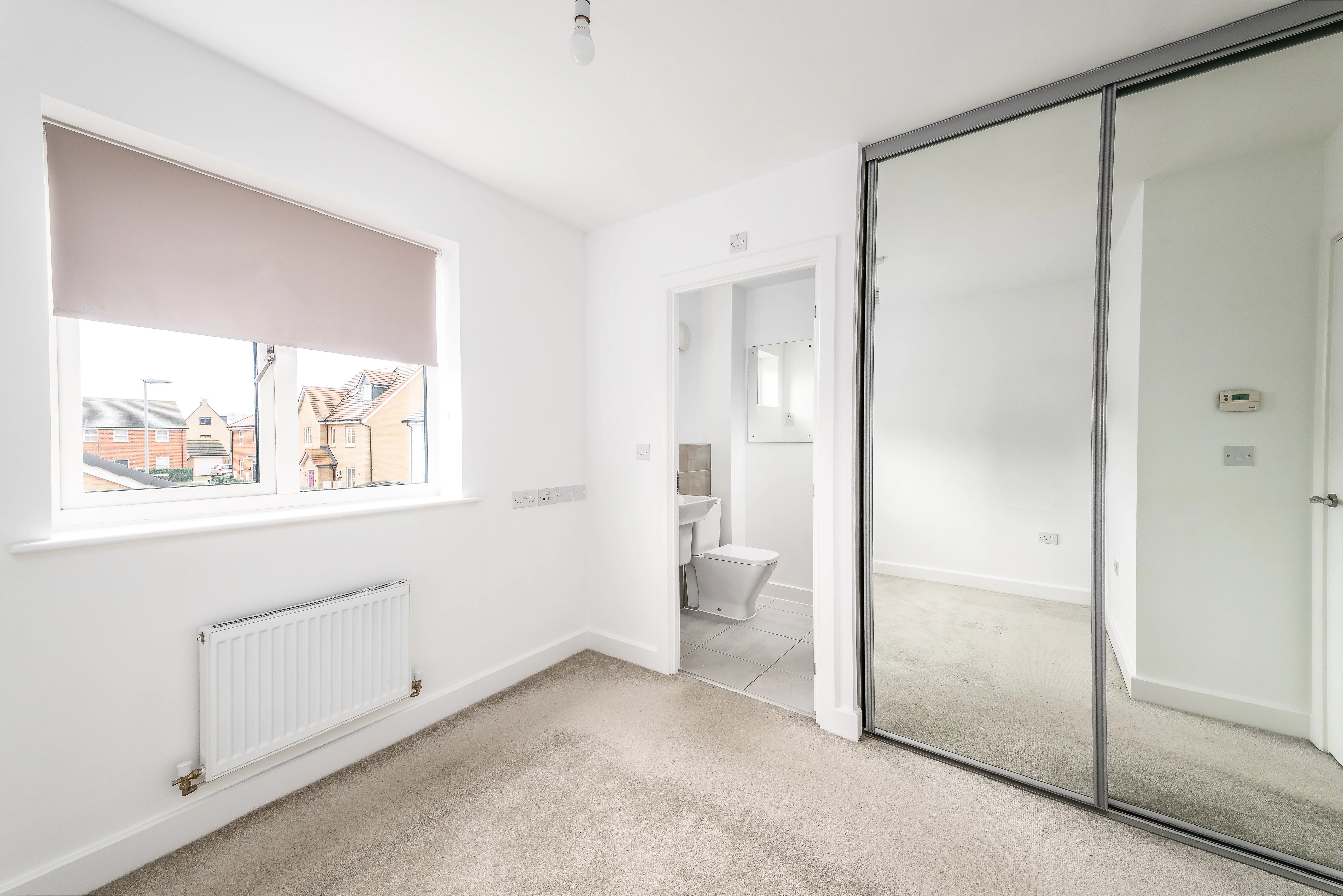 Interior of bedroom with mirror wardrobes and view into en-suite bathroom
