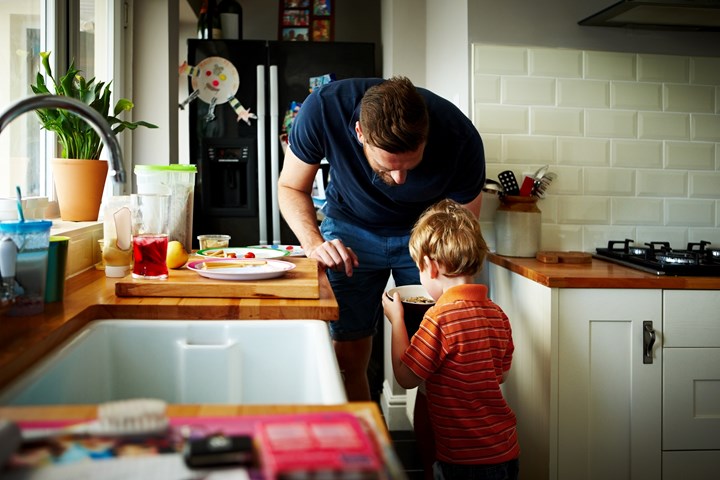 male figure in kitchen giving bowl of cereal to child