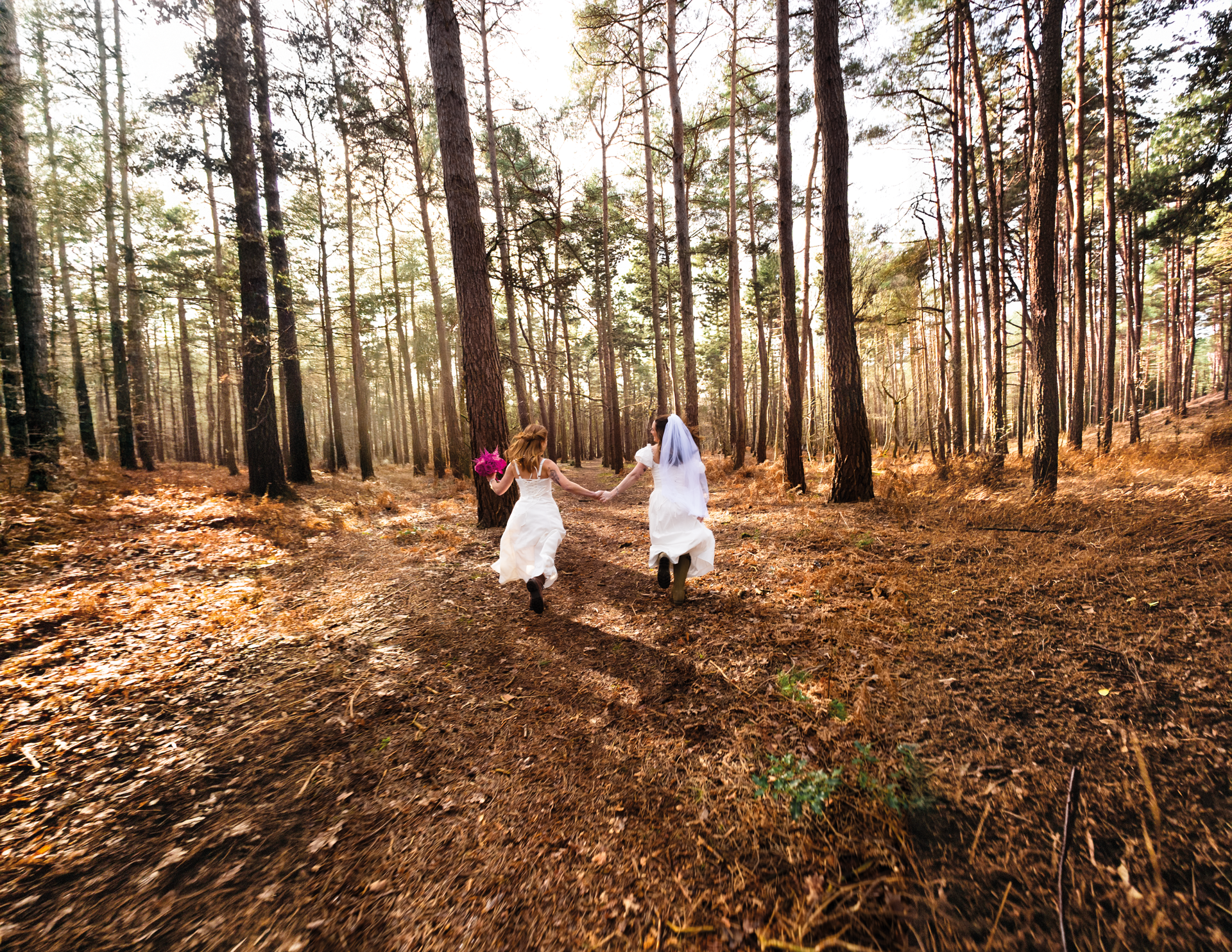 Mrs & Mrs running in a forest holding hands