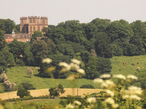 Hardwick Hall on a hill from a distance with trees in the foreground