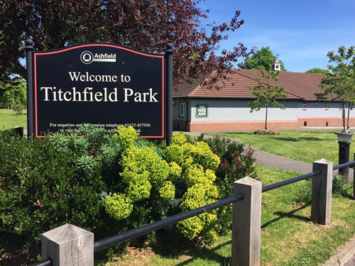 A Welcome to Titchfield Park sign surrounded by bushes and grassland