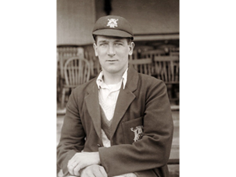 A black and white picture of Nottinghamshire cricketer Harold Larwood in a team blazer and cap.