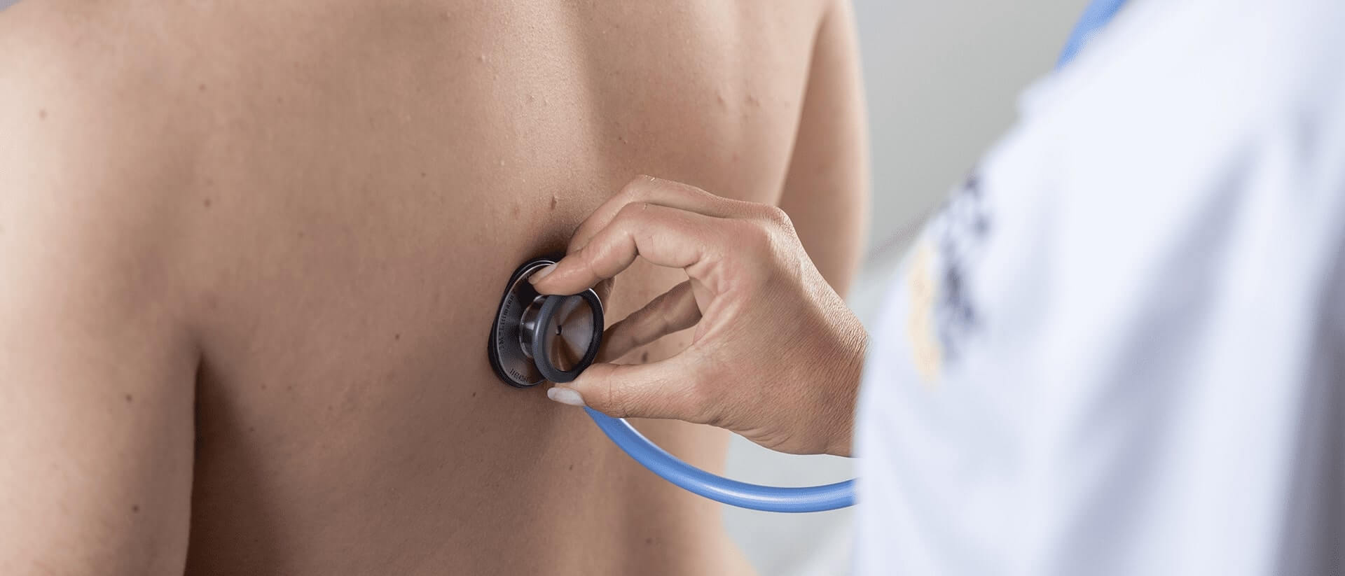 Doctor placing a stethoscope against a patient's back 