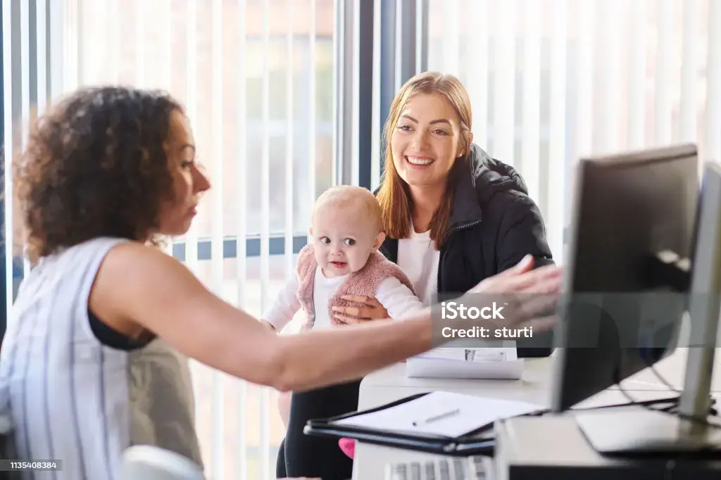 A woman with a baby on her lap talks to another woman on a computer.