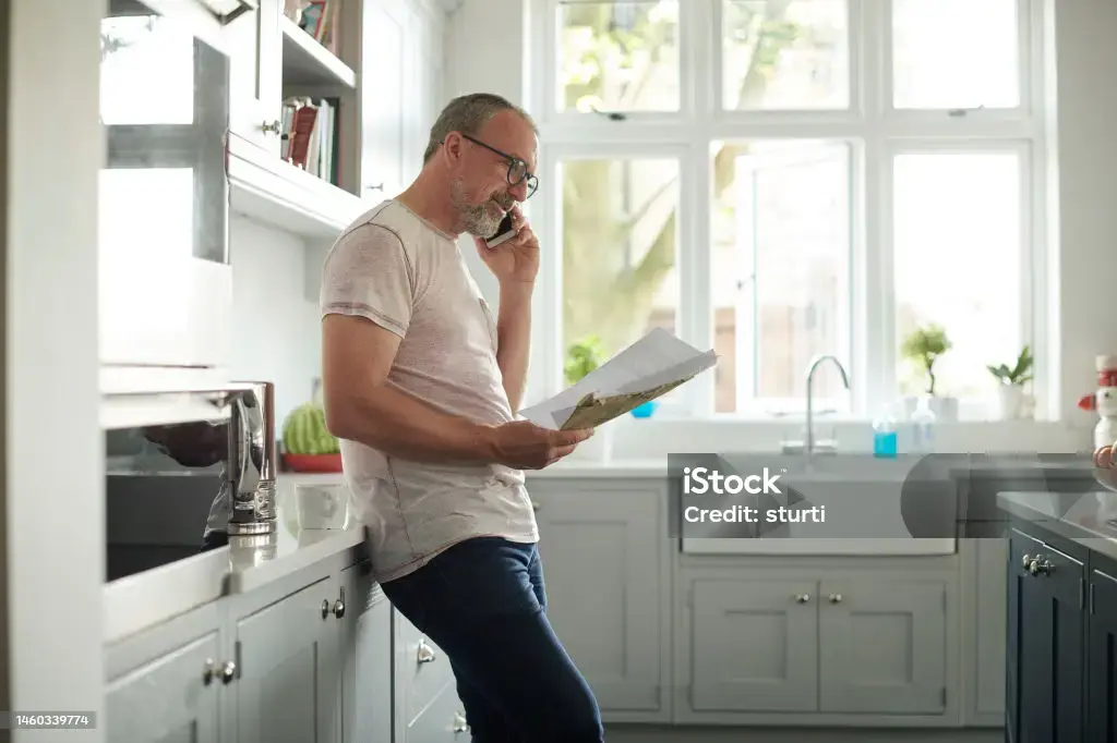 A man leans against his kitchen counter whilst on the phone.