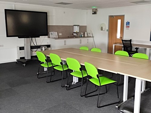 Kirkby in Ashfield Library meeting room with a projector screen, long table, and bright green chairs