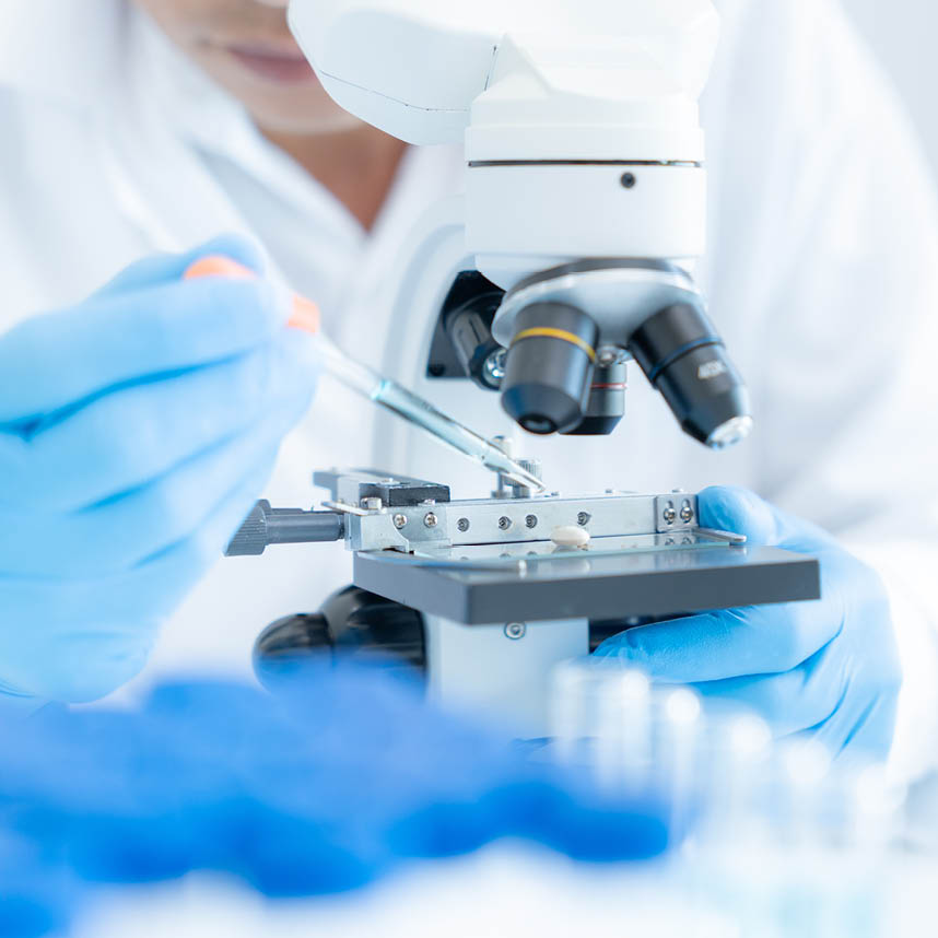 Scientist in protective gloves using a pipette and microscope in a medical laboratory.