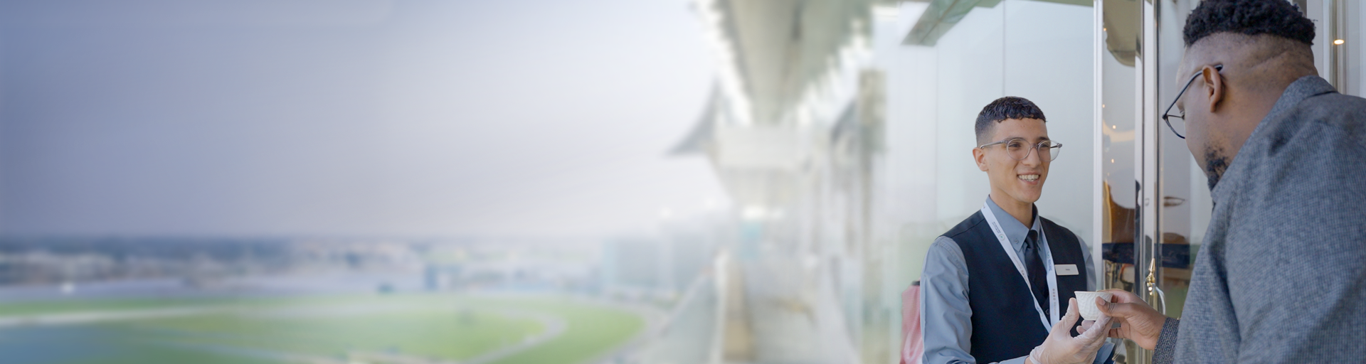 DWTC Hospitality staff serving a small cup to an event visitor with a racetrack in the background.