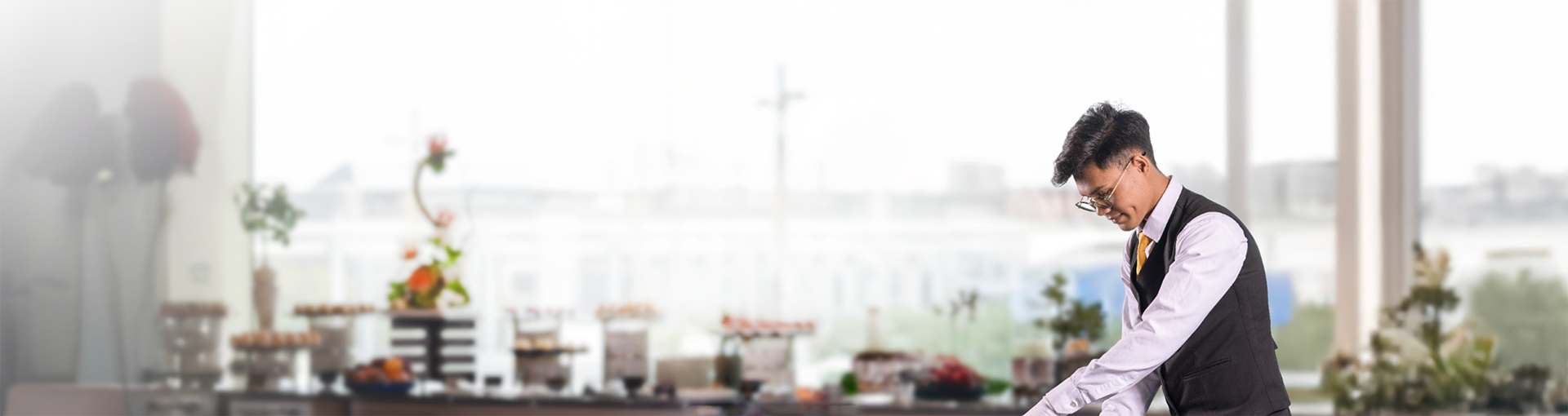 DWTC Hospitality waiter in black vest preparing an elegant buffet setup with decorative stands and a variety of food options.