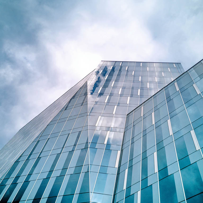 Modern glass office building with reflective windows against a cloudy sky.