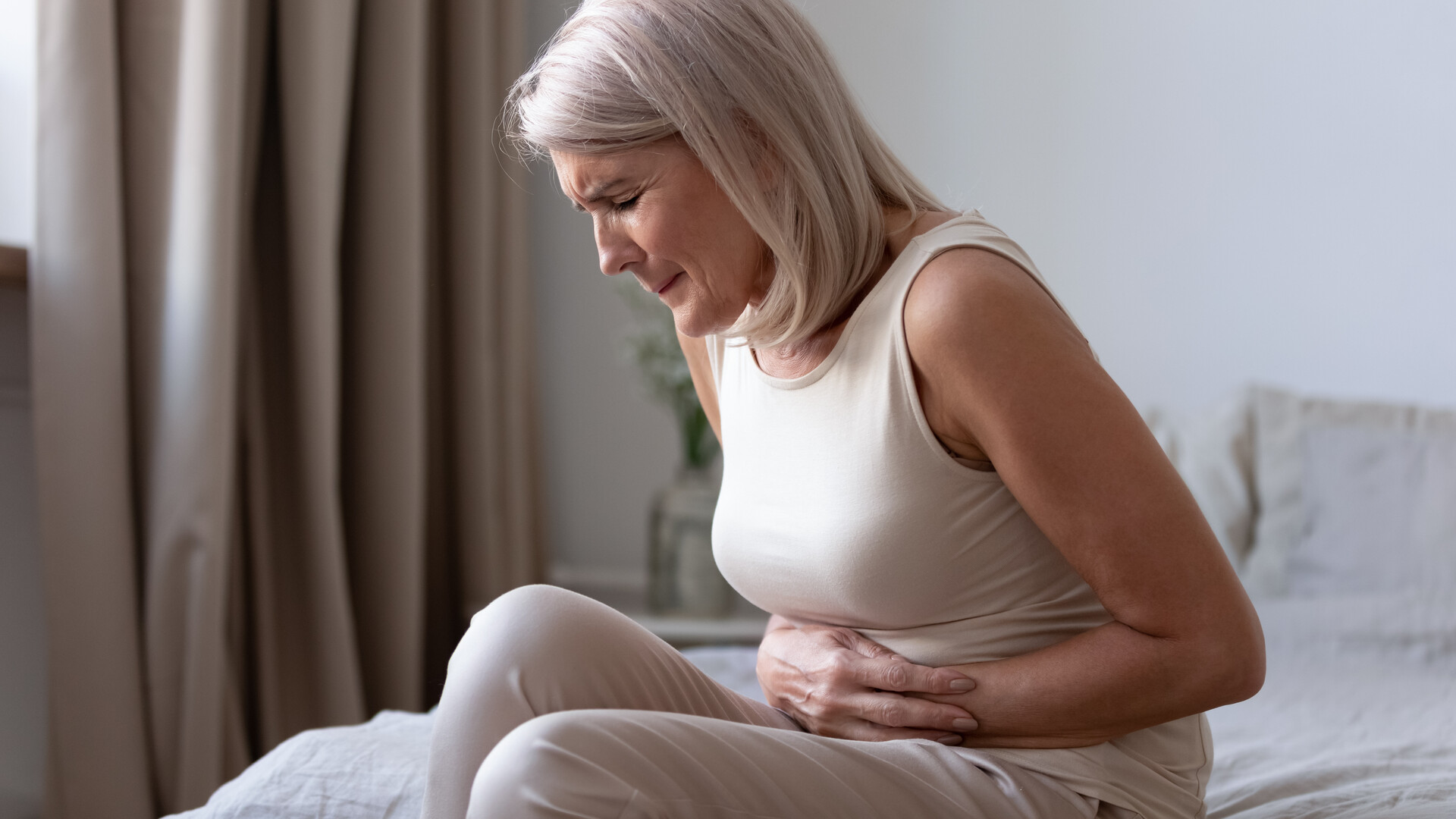 Mulher idosa sentada, com expressão de dor intensa, a segurar a zona abdominal