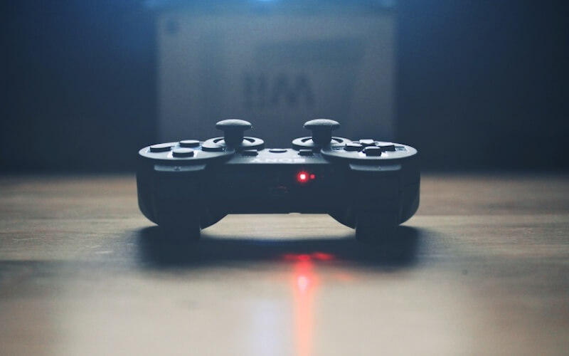 A black PS3 controller placed on a desk with a red light omitting from the top of the controller