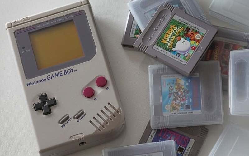 A grey gameboy console with several grey Gameboy cartridges next to it.