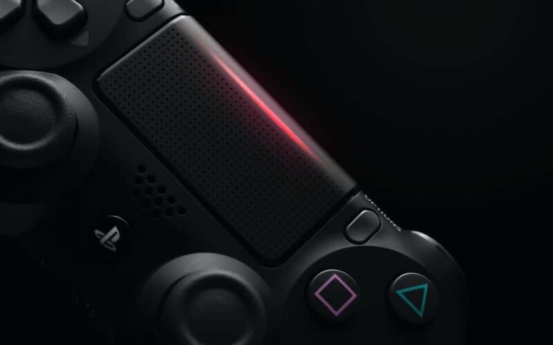 A black PS4 controller with a red light emitting from the centre of the controller
