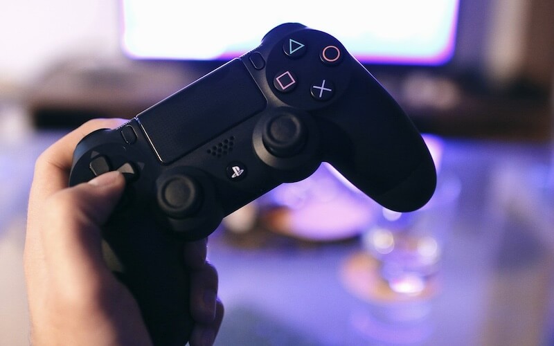 A hand holding a black PlayStation controller with a purple glowing screen in the background