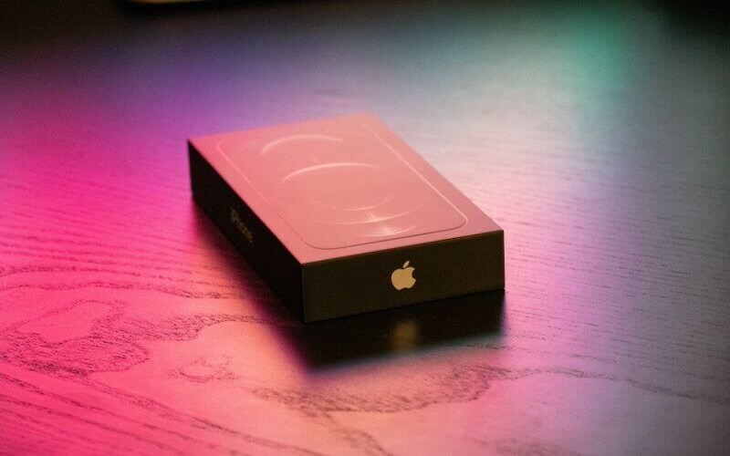 An iPhone box placed on a wooden table with colourful lights casting over it.