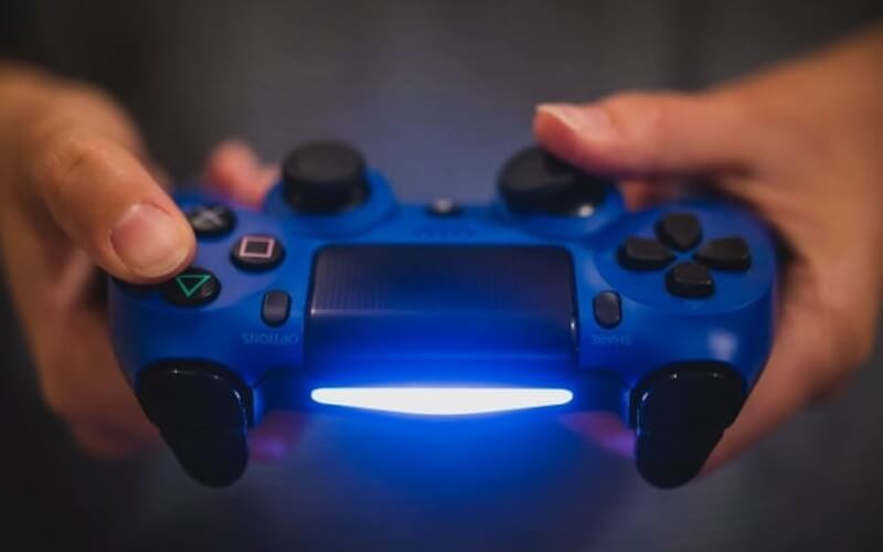 A person holding a dark blue PS4 controller in his hands, with thumbs on the triggers.
