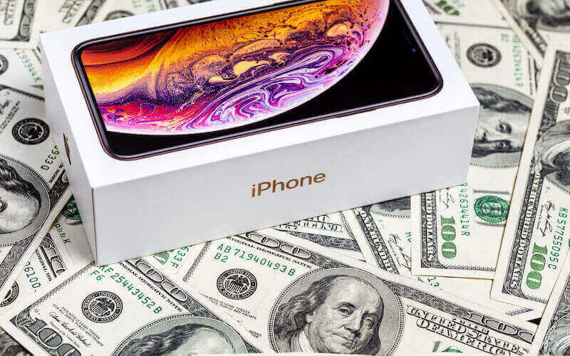 An iPhone box sat atop a table with dollar bills laid across it.