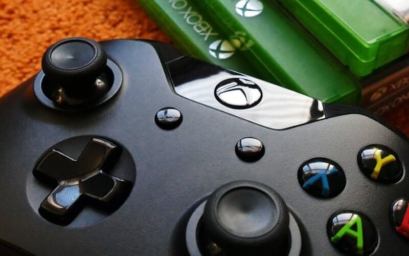 A close up of a black Xbox One controller with three green Xbox game cases laid next to the controller