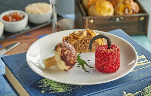 Photograph of a white plate with a green Peter Pan design on a table. The plate has a pepper, mushroom and savoury pastry on top.