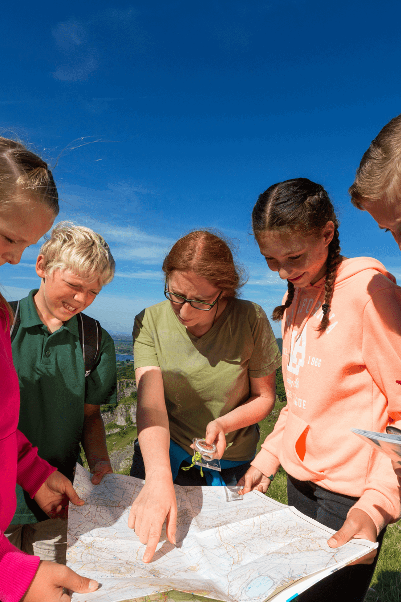 A group of students gather around an open map, whilst an instructor points out an area of interest