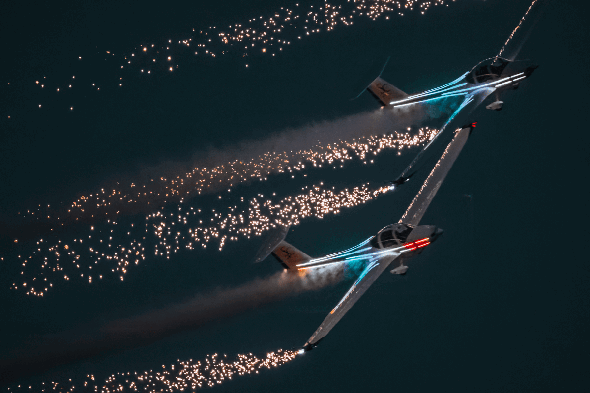 Two planes with neon lights fly in the night sky with lights trailing behind them