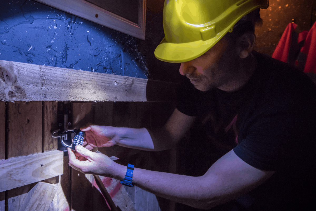 A man in a dark room wearing a hard hat focuses on unlocking a padlock with a 4 digit code