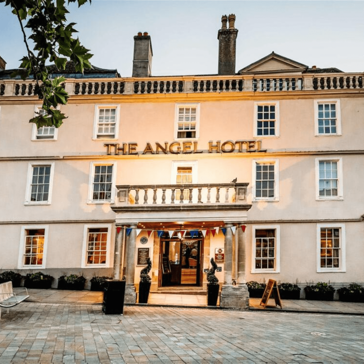 The Angel Hotel - A large white hotel building with pillars at the entrance and outdoor lighting.