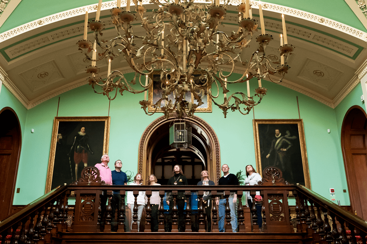 A group of visitors stand at the top of the staircase to look up at the grand chandelier on a guide tour of Longleat House