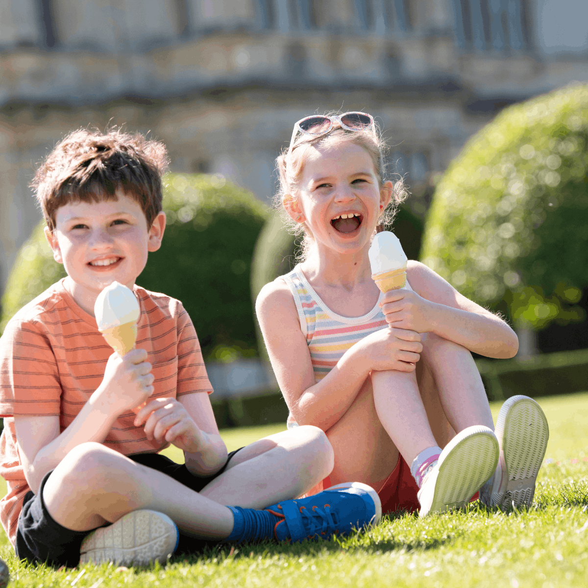 A young  boy and girl sitting on grass and eating ice cream