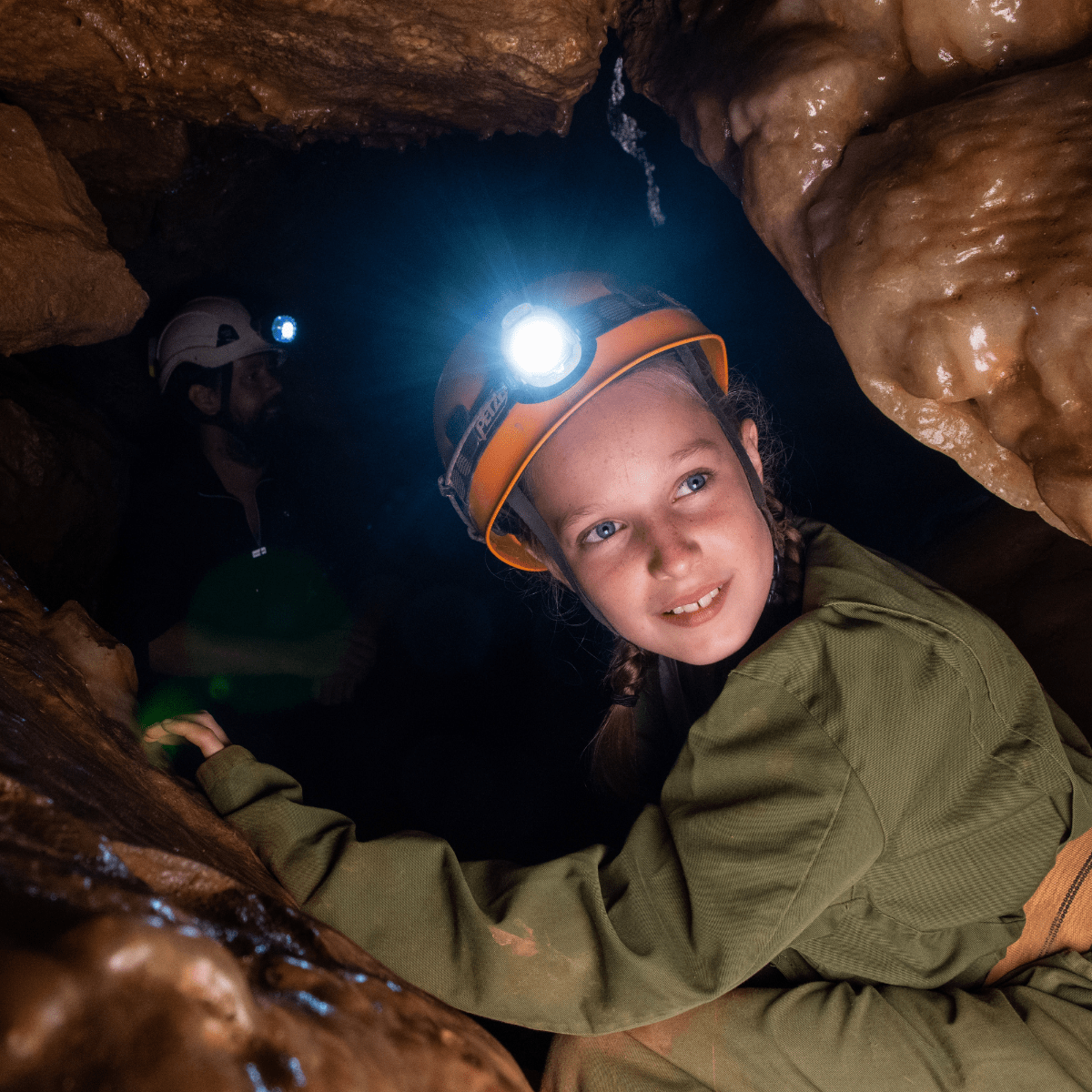 A young girl enjoys adventure caving as she turns to the camera with her head torch on show