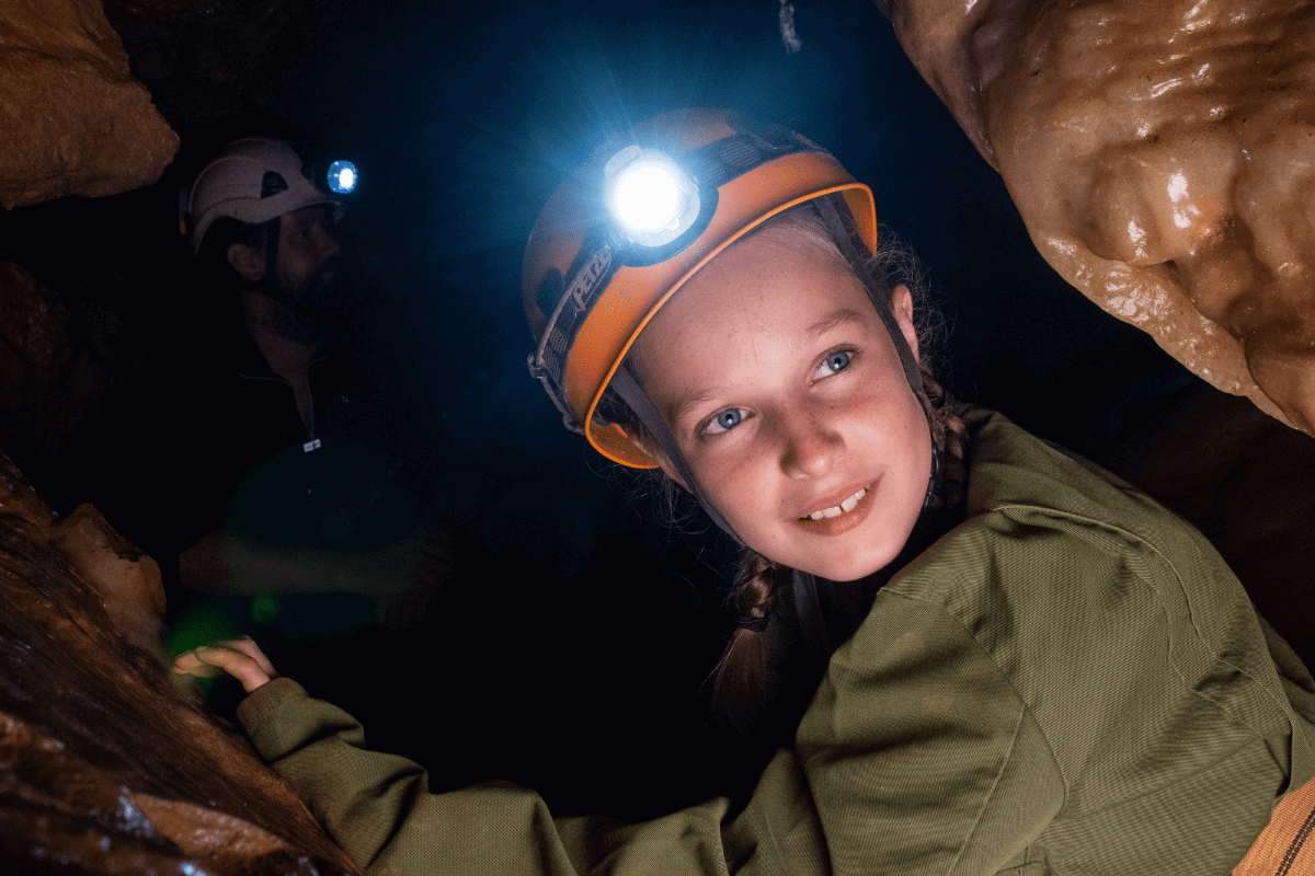 A young girl enjoys adventure caving as she turns to the camera with her head torch on show