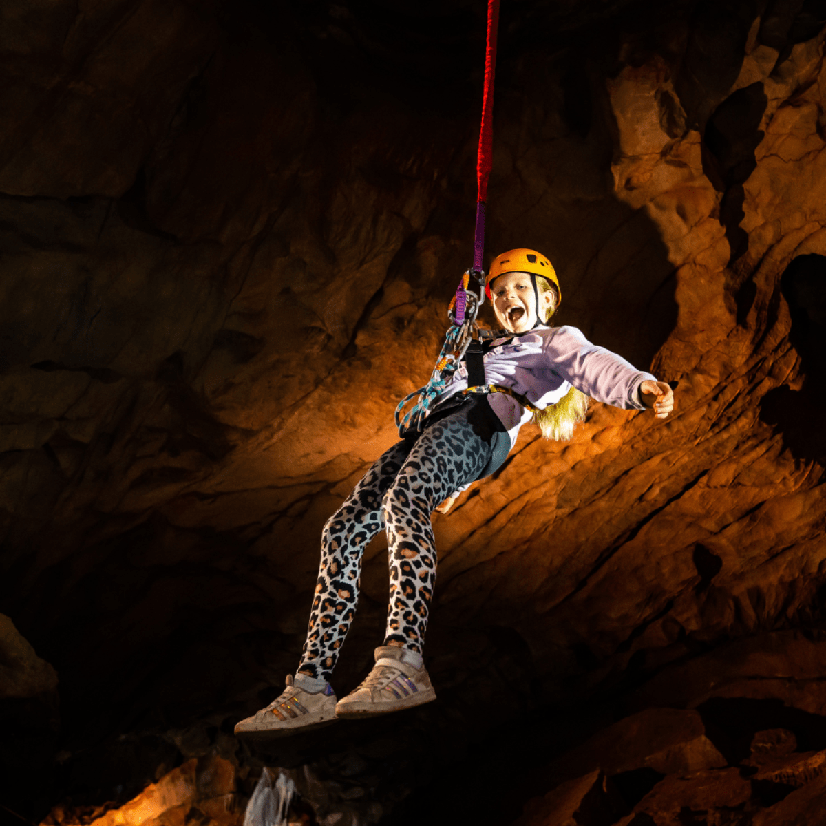 A young girl experiencing the Black Cat Freefall challenge with a bright smile on her face as she is suspended in the cave