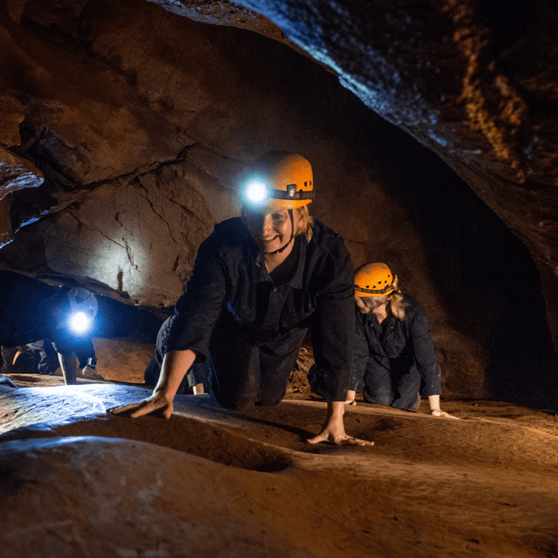 A group of people enjoying adventure caving at Cheddar as they crawl on their hands and knees with head torches lighting their way