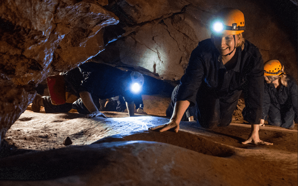 A group of people enjoying adventure caving at Cheddar as they crawl on their hands and knees with head torches lighting their way