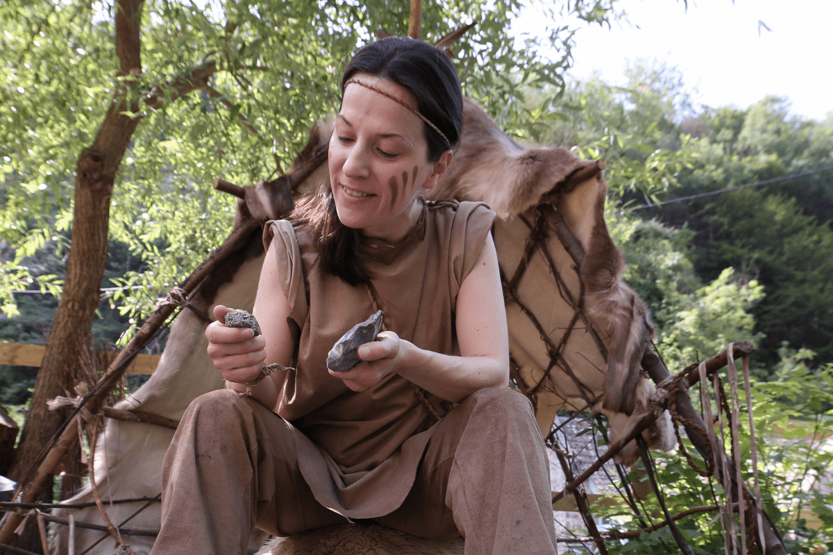 An actor demonstrates flint knapping whilst wearing prehistoric clothing