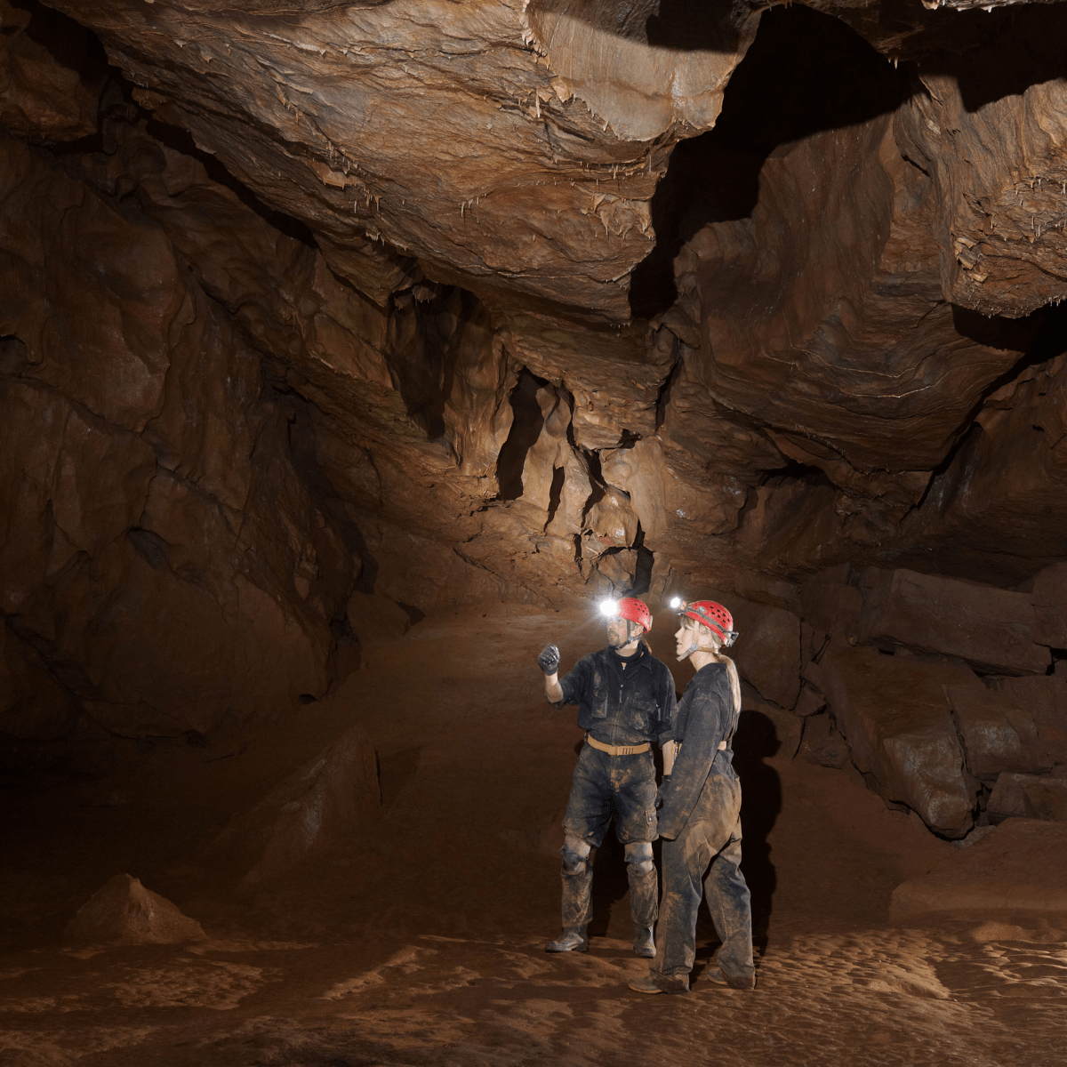 Two adventure cavers look around the cave with their head torches lighting up the cave's rocky walls