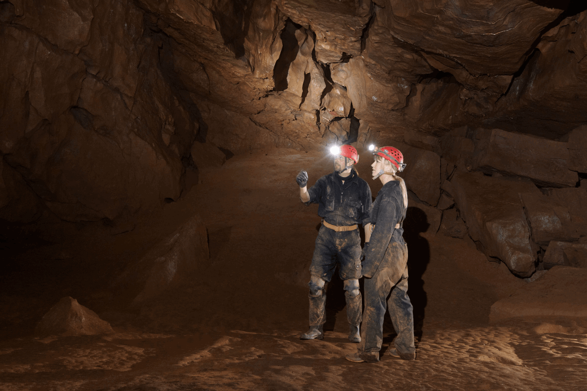 Two adventure cavers look around the cave with their head torches lighting up the cave's rocky walls