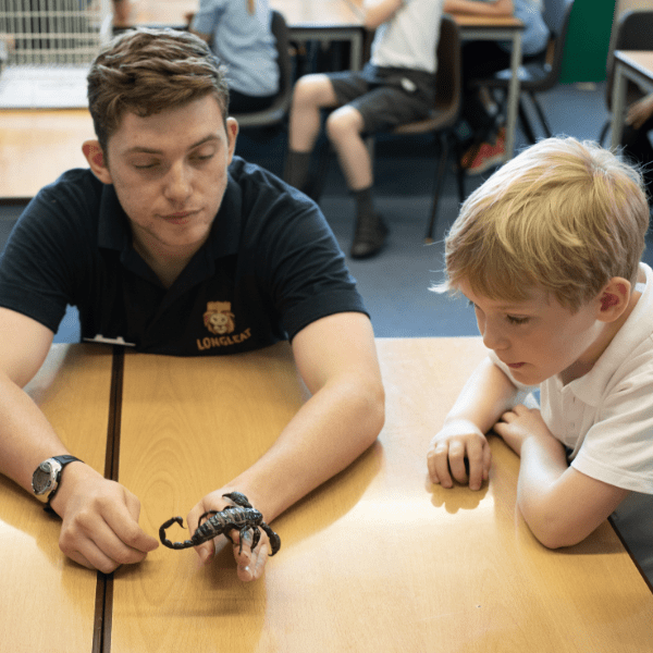 A scorpion being held by a keeper in a classroom as a schoolchild looks on