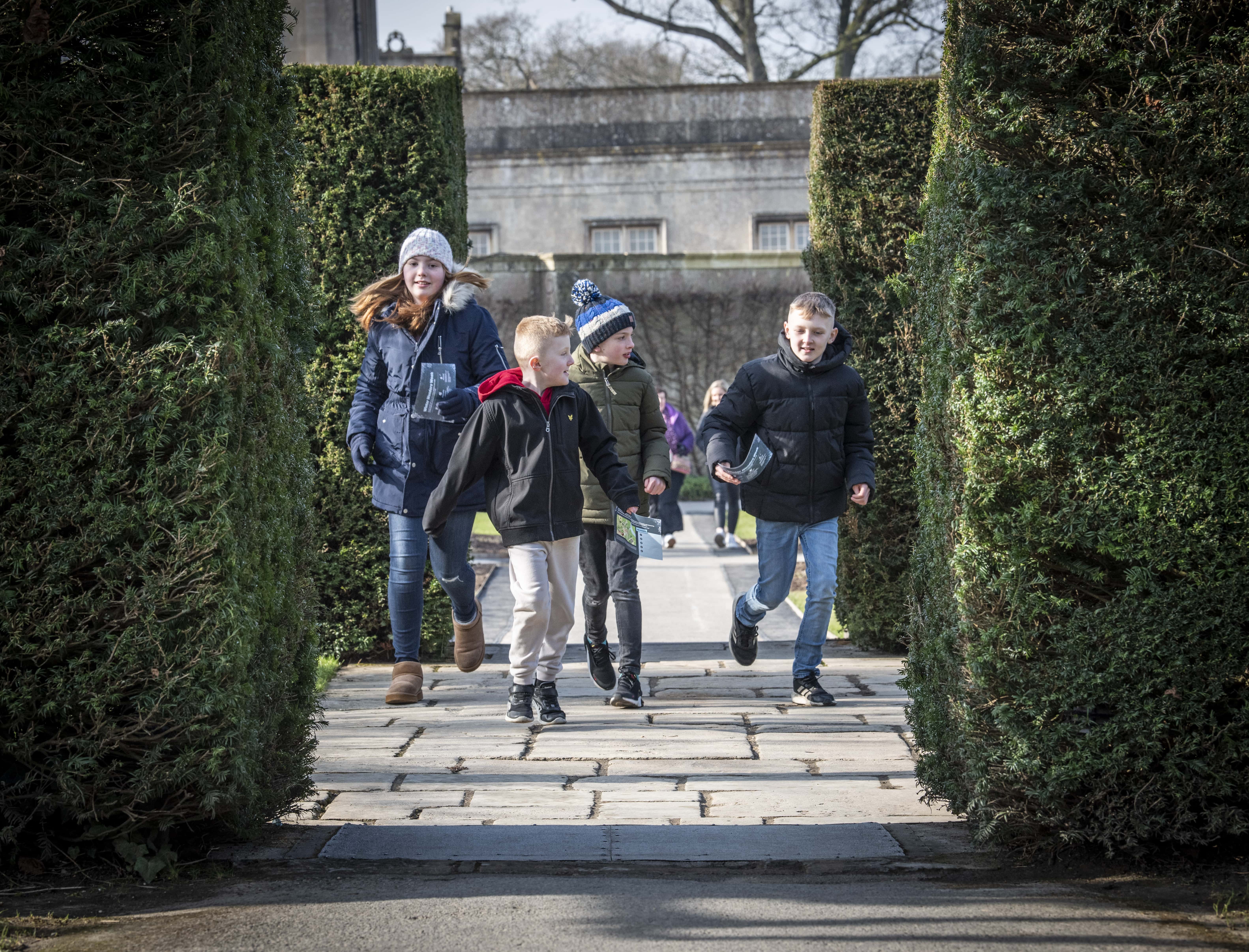 A group of children in wintery clothing run together towards the camera in Longleat Gardens