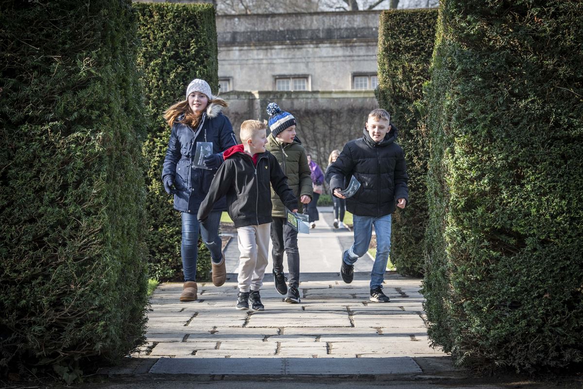 A group of children in wintery clothing run together towards the camera in Longleat Gardens