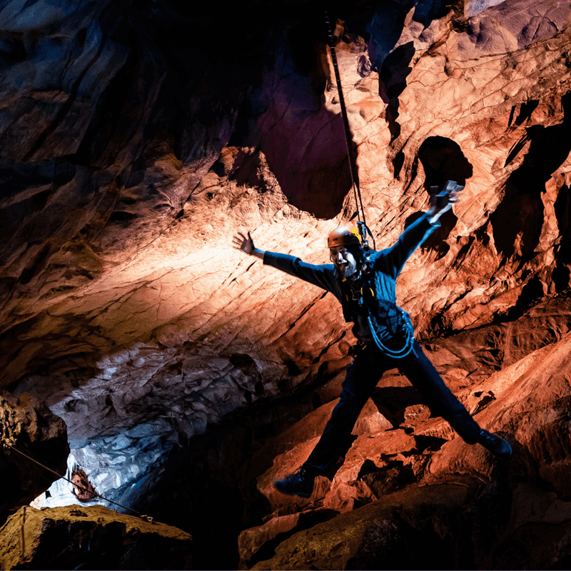 A visitor at Cheddar Gorge, enjoying the Black Cat Freefall activity, as they hang in the cave with limbs outstretched and a huge grin