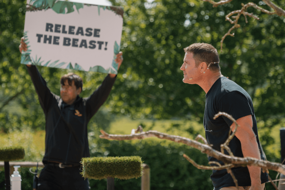 Side view of Steve Backshall performing a live show with a man holding up a sign saying "Release the beast!" in the background