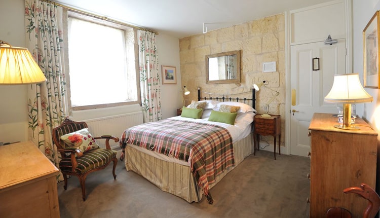 Woolley Grange Hotel - A bedroom with a double bed with tartan blanket, wooden furniture and table lamps