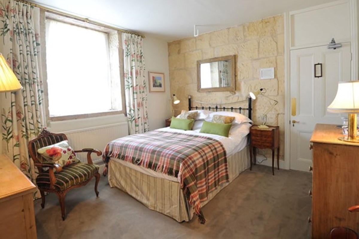 Woolley Grange Hotel - A bedroom with a double bed with tartan blanket, wooden furniture and table lamps