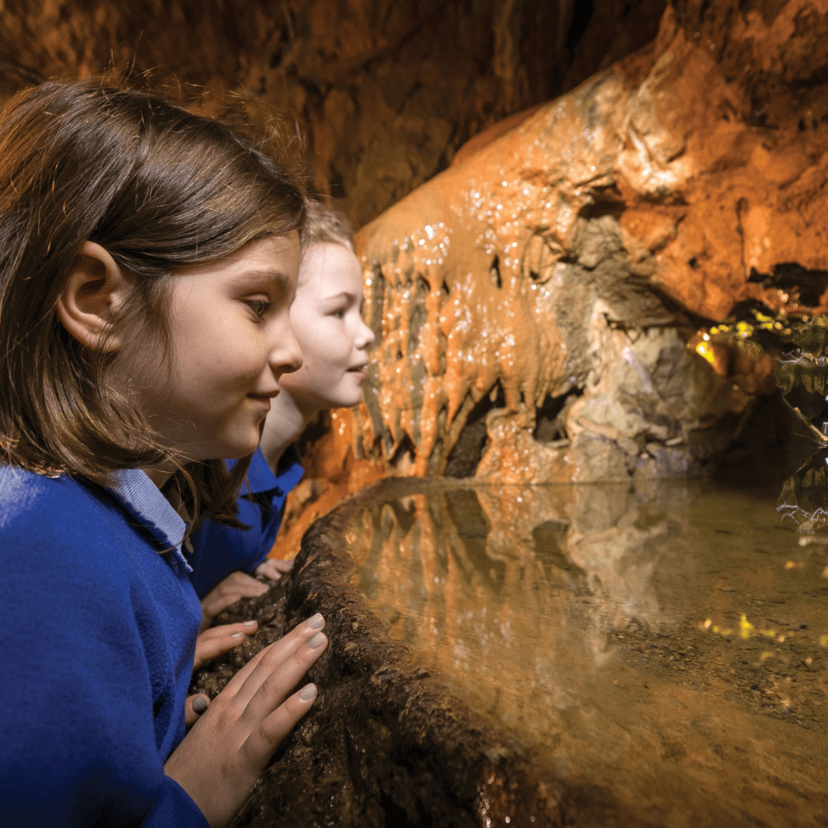 Two young school students peer in to one of the impressive water pools with stalagmites inside of Gough's Cave 