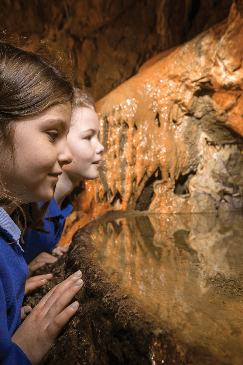 Two young school students peer in to one of the impressive water pools with stalagmites inside of Gough's Cave